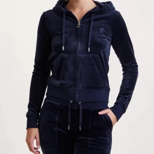 Mörkblå velour sett från Juicy Couture - Säljer en mörkblå sett från Juicy Couture i mjuk velour med huva och snörning. Tröjan har dragkedja framtill, ribbade muddar och fickor. Perfekt för chill dagar eller när du vill vara extra comfy.