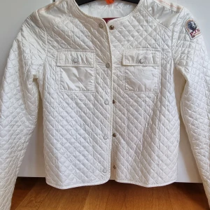 Vit quiltad jacka från Parajumpers - Säljer en snygg vit quiltad jacka från Parajumpers med två bröstfickor och tryckknappar framtill. Jackan har lång ärm, rund halsringning och klassisk PJS-logga på axeln. Perfekt för dig som vill ha en stilren och lätt jacka med coola detaljer.  Y s = storlek 158 ( ca 30,32 i vuxen) 