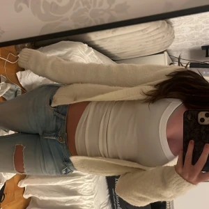 Vit kofta från Holly & Whyte XS - Supermjuk och fluffig vit kofta från Holly & Whyte i storlek XS. Koftan har snygga guldknappar framtill, två fickor och ribbade kanter. Perfekt för lager-på-lager och ger en clean och cozy vibe till din outfit.