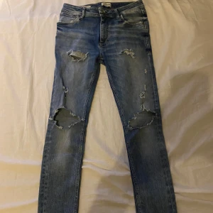 Rippade skinny jeans Jack & Jones - Snygga ljusblå skinny jeans från Jack & Jones med slitna detaljer och stora hål på knäna. Klassisk femficksmodell med normal passform i midjan och smala ben. Perfekta för dig som gillar en trendig och avslappnad look.