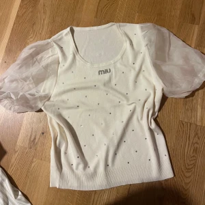 Vit topp med puffärmar från Miu Miu - Supersöt vit topp från Miu Miu med transparenta puffärmar i organza och små glittriga stenar över hela framsidan. Toppen har rund halsringning och en mjuk, stickad känsla i kroppen. Perfekt för dig som vill sticka ut lite extra. Passar xs och s, SUPERSKÖNT OCH MJUKT MATERIAL!! 
