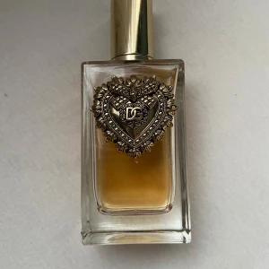 Dolce & Gabbana Devotion EdP 100ml - Lyxig parfym från Dolce & Gabbana, Devotion Eau de Parfum, 100 ml. Flaskan är rektangulär i tjockt glas med guldig metallkork och en detaljerad hjärtformad dekoration framtill med DG-logga. Innehållet är bärnstensfärgat och flaskan känns riktigt exklusiv.75-80 ml kvar 