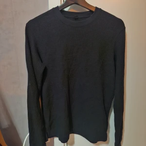 Svart långärmad tröja från Uniqlo XS - Svart långärmad tröja från Uniqlo i storlek XS. Tröjan har en enkel, stilren design med rund hals och ett diskret rutigt strukturmönster i materialet. Perfekt för lager-på-lager och passar till allt. Superenkel att matcha med jeans eller kjol.