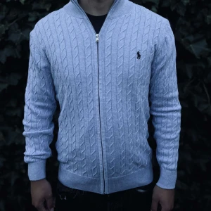 Ljusblå kabelstickad kofta Polo Ralph Lauren - Snygg ljusblå kabelstickad kofta från Polo Ralph Lauren med dragkedja framtill och klassisk logga på bröstet. Tröjan har ribbade muddar och hög krage, perfekt för lager-på-lager. Passformen är normal och materialet känns mjukt och skönt..      Nypris: 3145kr GORILLAPRIZE:1680kr             Skick:10/10 oöppnad          KVITTO MEDKOMMER 