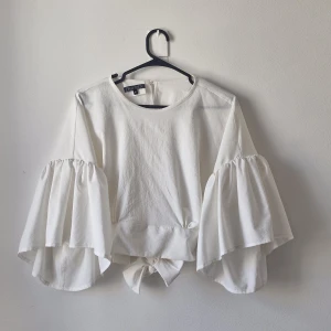 Vit blus med volangärmar från Charlotte - Blus från märket Charlotte med vida volangärmar och knytning i midjan. 