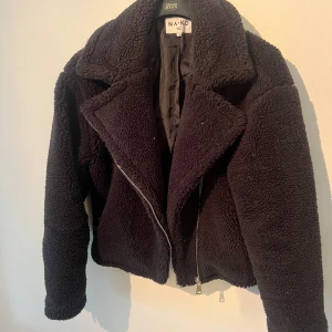 Svart teddyjacka från NA-KD, stl 36 - Mysig svart teddyjacka från NA-KD i storlek 36. Jackan har en bred krage, dragkedja framtill och är tillverkad i fluffigt teddy-material som håller dig varm. Perfekt för kyliga dagar och ger en cool vibe till din outfit.