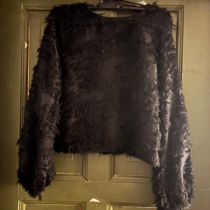 Svart fluffig blus med öppen rygg - Cool svart blus  med fluffig textur och croppad passform och även ganska genomskinlig . Toppen har långa ärmar och en snygg öppen rygg med knytband i nacken. Perfekt för dig som vill sticka ut med en unik look. 