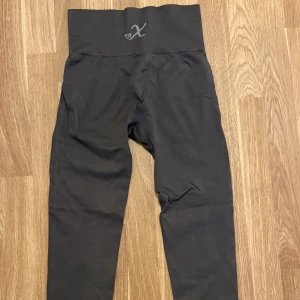 Svarta höga seamless leggings Xshapes - Säljer ett par mörkgrå leggings med hög midja och bred resår. De är sömlösa och har en diskret logga baktill i midjan. 