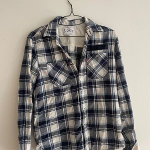Rutig skjorta från Levi's, blå/vit S - Snygg rutig skjorta från Levi's i blått och vitt. Klassisk modell med två bröstfickor, knappar framtill och lång ärm. Perfekt för dig som gillar avslappnad stil med en touch av vintage. Skön bomullskänsla och tidlös design.