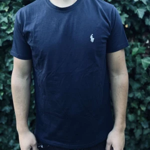 Mörkblå t-shirt från Polo Ralph Lauren - Snygg mörkblå t-shirt från Polo Ralph Lauren med klassisk vit broderad logga på bröstet. T-shirten har rund hals, korta ärmar och är gjord i mjuk bomull som känns skön mot huden. Perfekt för dig som gillar stilrena och tidlösa plagg.                                                                                                                                                                   Nypris:699kr GORILLAPRIS:349kr              Skick: 10/10 Oöppnad                KVITTO MEDKOMMER