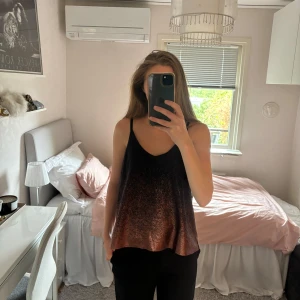 Skimrande topp - Linne med smala axelband, skimrande och metallic effekt i orange/brun/brons färg. Står storlek s på lappen men skulle säga att den är mer som storlek M, 100% polyester.  Skriv om du har några frågor🩷