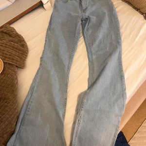 Ljusblå bootcut jeans med slits - Säljer ett par ljusblå jeans med bootcut passform och slits nertill på benen. Jeansen har klassisk femficksdesign och är tillverkade i mjukt denimtyg. Perfekta för dig som gillar en avslappnad och trendig look.