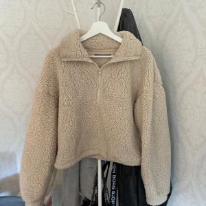 Beige fleece-tröja från BikBok - Supermjuk och fluffig beige fleece-tröja från BikBok med halv dragkedja och hög krage. Perfekt för kyliga dagar, har en loose passform och långa ärmar. Snygg att styla med jeans eller leggings för en chill look.