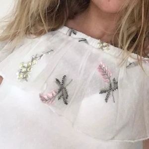 Vit offshoulder blus med broderi XS - Superfin vit offshoulder blus från Divided i storlek XS. Toppen har volang upptill och är dekorerad med broderade blommor i rosa, gul och grå. Tunn och luftig mesh med elastisk kant upptill för perfekt passform. Använd 1 gång💕☺️