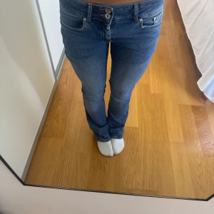 Blå jeans med broderade fjärilar - Snygga blå jeans med raka ben och låg midja. Baktill finns två fickor med broderade fjärilar som ger en unik touch. Jeansen har dubbla knappar framtill och klassisk femficksdesign. Perfekta för dig som vill ha något extra i vardagen.