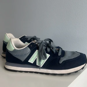 Mörkblå New Balance sneakers 500 storlek 38 - Snygga New Balance sneakers i mörkblå mocka och mesh med ljusgröna detaljer och blå snörning. Skorna har en klassisk siluett med rund tå, vit sula och bekväm passform. Knappt använda, lite för små. 