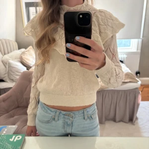 Beige stickad blus med volang - Supersöt beige stickad blus med långärmade spetsdetaljer och stor volang runt axlarna. 