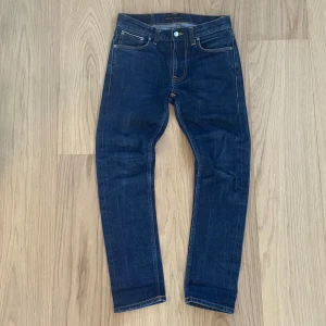 Nudie Jeans Lean Dean blå jeans - Hej, säljer ett par Nudie Jeans Lean Dean i mörkblå japan selvage denim med klassiska orange sömmar och snygg broderad bakficka. Storlek 28/30. Modellen är slim och tillverkad i 98% bomull och 2% elastan. Perfekta jeans för dig som gillar en smalare passform.