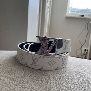 Vit Louis Vuitton monogram skärp - Snyggt vitt Louis Vuitton bälte med klassiskt monogrammönster i ljusgrått och stor LV-logga i silvermetall som spänne. Bältet är gjort i präglat skinn och har en stilren, modern look som sticker ut.