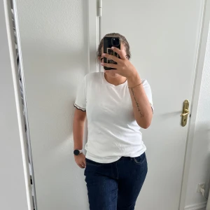 Vit t-shirt med spetsdetalj från Zara - Vit t-shirt från Zara med korta ärmar och snygga spetsdetaljer i svart och guld vid ärmsluten. Rund halsringning och skön passform i mjuk bomull. Perfekt för dig som gillar en enkel stil med en twist.