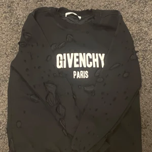 Svart Givenchy sweatshirt med tryck - Svart sweatshirt från Givenchy med stort vitt logotryck på bröstet. Tröjan har distressed detaljer över hela ytan för en edgy look. Klassisk rund hals och långa ärmar. Perfekt för dig som gillar streetstyle och designerplagg.
