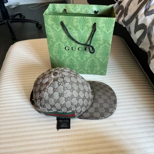 Gucci keps med monogrammönster - Säljer en klassisk Gucci keps med brunt monogrammönster och gröna/röda detaljer baktill. Kepsen har böjd skärm och är tillverkad i ett slitstarkt tyg med tydlig logotyp. Perfekt accessoar för dig som gillar exklusiva märken.