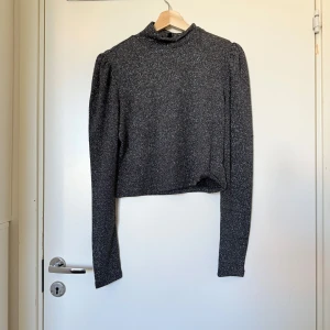 Glittrig croppad polotröja från Divided - Säljer en glittrig mörkgrå croppad polotröja från Divided. Tröjan har långa ärmar och en hög krage, perfekt för att lyfta vilken outfit som helst. Materialet är stretchigt och skimrar snyggt i ljuset. Storlek L. Mycket fint skick, jag hittar inga synliga anmärkningar eller defekter. 