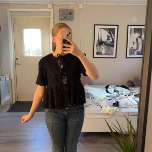 Svart blus med knyt från Gina Tricot - Svart blus från Gina Tricot med tre dekorativa knyt framtill. Blusen har korta puffärmar och ett strukturerat tyg som ger en snygg effekt. Passar perfekt till jeans eller kjol för en trendig look. Tröjan är i stolek small. 🖤🍾