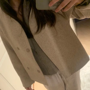 Beige ullkappa från Gina Tricot - Säljer en stilren beige kappa från Gina Tricot i ullblandning. Jackan har dubbelknäppning framtill, klassisk krage och raka ärmar. Perfekt för dig som gillar en enkel och tidlös look.