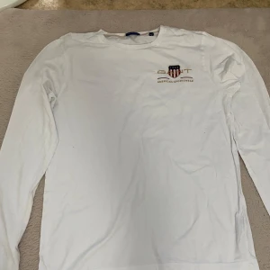 Vit långärmad tröja från GANT - Säljer en klassisk vit långärmad tröja från GANT med liten logga och text på bröstet. Har aldrig kommit till användning hos oss.