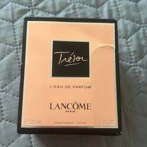 Trésor L'Eau de Parfum från Lancôme - Trésor L'Eau de Parfum från Lancôme i en elegant, diamantformad glasflaska med klar och svart detalj. Parfymen är 30 ml och kommer i en persikofärgad och svart kartong. En klassisk och feminin doft från ett välkänt franskt parfymmärke. Endast testad. 