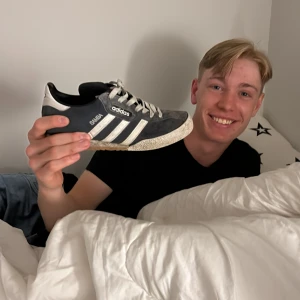 Adidas Samba sneakers i svart och vitt - Klassiska Adidas Samba sneakers i svart mocka med vita läderdetaljer och tre vita ränder på sidan. Skon har gummisula och rund tå, samt Adidas-logga och Samba-tryck i vitt på sidan. Perfekt för dig som gillar retrostil och streetwear.