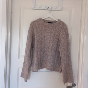 Beige stickad tröja från Lager 157 - Mysig beige stickad tröja från Lager 157 i storlek S. Tröjan har ett klassiskt flätmönster och ribbade muddar vid hals, ärmslut och nederkant. Perfekt för kyligare dagar och enkel att matcha med olika outfits.