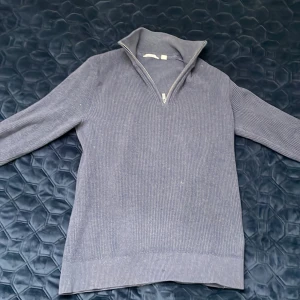 Grå ribbad tröja med dragkedja - Säljer en stilren grå ribbad tröja med halv dragkedja i halsen. Tröjan har lång ärm och hög krage som kan vikas ner. Perfekt för lager-på-lager och passar till många olika outfits.