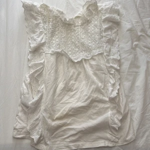 Vit blus med spets och volang från MNG - Säljer en söt vit blus från MNG med spetsdetaljer upptill och längs sidorna. Blusen har volanger och v-ringning både fram och bak. Perfekt för dig som gillar romantisk stil och fina detaljer. Knappen där bak är sönder därav priset