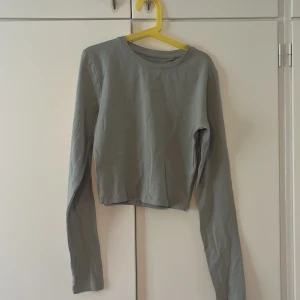 Ljusgrå croppad långärmad topp  - Säljer en stilren ljusgrå croppad långärmad topp med rund halsringning. Perfekt att matcha med höga jeans eller kjol. Tunt och mjukt bomullsliknande material som känns skönt mot huden. Och är oanvänd 