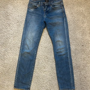 Blå Studio Relaxed jeans från Neuw - Säljer ett par blå jeans från Neuw i modellen Studio Relaxed. Jeansen har klassisk femficksdesign, raka ben och normal passform. Perfekta för dig som gillar någonting mellan slim fit och straight fit. Snygga slitningar och detaljer i orange söm.