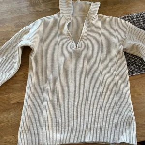 Beige ribbad stickad tröja med dragkedja från SHEIN - Säljer en beige stickad tröja från SHEIN i storlek S. Tröjan har ribbad struktur, hög krage och dragkedja framtill. Perfekt för lager-på-lager och enkel att matcha med olika outfits.