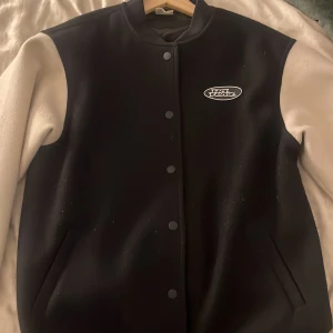 Svart och vit varsityjacka från No Fun/H&M - Säljer en svart och vit varsityjacka från No Fun med tryckt logga på bröstet och stor logga på ryggen. Jackan har långa vita ärmar, svarta fram- och bakstycken samt knäppning med svarta knappar. Tillverkad i polyester.