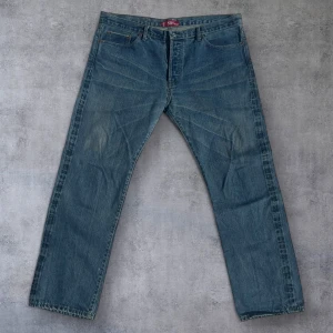 Levi's 501 jeans W40 L34 - Klassiska blå Levi's 501 jeans med raka ben och knappgylf. Tillverkade i 100% bomull och har en vintagekänsla med tydliga slitningar. Modellen har normal passform och är i storlek W40 L34. Perfekta för dig som gillar tidlös denimstil.