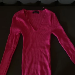 Rosa ribbad blus långärmad från Newyorker - Säljer en snygg ribbad blus långärmad  från Newyorker i stark rosa färg. Blusen har lång ärm och djup v-ringning, figurnära passform och stretchigt material. Perfekt för dig som vill sticka ut med färg. Obs har aldrig använt den men prislappen togs bort för användning men blev aldrig en användning för den