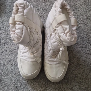Vita vinterboots med storlek 40 - Säljer ett par chunky vita vinterboots med snörning och grov sula. Skorna har vadderat skaft och detaljer i syntetmaterial. Perfekta för kalla dagar när du vill hålla fötterna varma och samtidigt ha en cool stil.