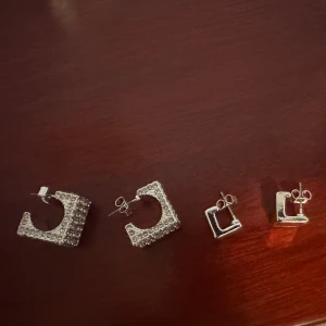 Två par fyrkantiga örhängen i silver - Säljer två par helt nya (aldrig använda alls) fyrkantiga örhängen i silverfärg. Ett par är större och täckta med glittrande stenar, medan det andra paret är mindre och släta. Perfekta för att variera din stil! Säljs som ett sätt (båda 2)= 80kr, eller en för 45kr☺️ kan mötas upp i stockholm eller posta, men står ej för frakt!