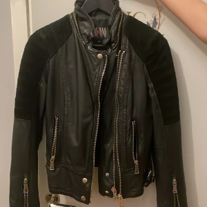 Svart skinnjacka från Jofama x Rookie - Säljer en svart skinnjacka från Jofama x Rookie i storlek 34. Jackan har snygga detaljer med dragkedjor, axelpartier i mocka och ett broderat ros-motiv på insidan. Perfekt för dig som vill ha en cool och unik jacka.
