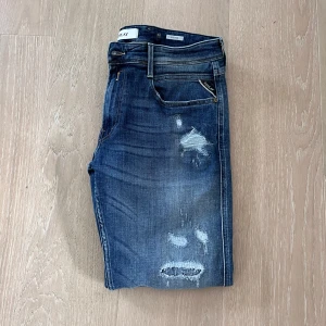 Replay Anbass - Säljer ett par blå Replay jeans med snygga slitningar. Jeansen har klassisk femficksdesign, läderpatch med Replay-logga bak och diskreta detaljer. Perfekta för en avslappnad och trendig look.