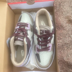Nike scraps sneakers  - Säljer ett par fräscha Nike sneakers i beige, lila och bruna toner. Skorna har klassisk Nike-logga på sidan, perforerad tå och vita sulor. Snygga kontrastdetaljer och sköna att bära till vardags. Kommer i originalkartong.