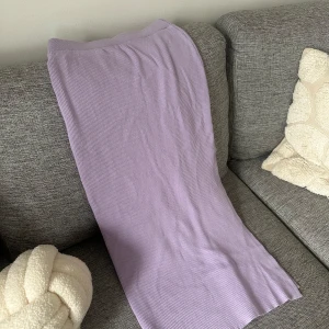 Ljuslila ribbad långkjol med slits  - Säljer en ljuslila långkjol med ribbad struktur och slits. Kjolen har en elastisk midja och är figurnära i modellen. Perfekt för dig som gillar en enkel men trendig stil.