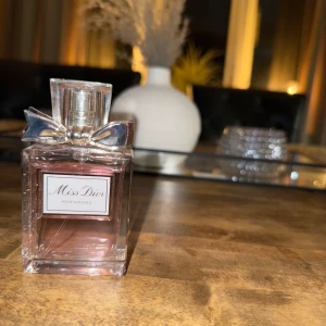 Miss Dior Eau de Parfum - ENDAST TESTAD! En elegant parfymflaska från Dior med ljusrosa vätska. Flaskan är rektangulär med ingraverat mönster och har en silverfärgad rosett vid halsen. Lock i genomskinlig plast. Perfekt för dig som gillar lyxiga och feminina dofter.✨