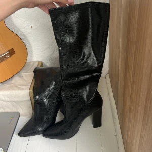 Svarta stövletter med spetsig tå - Snygga svarta boots i skinn med spetsig tå. Perfekta för en stilren look. Dem är ca 10cm höga med en tjockare klack, super snygga med orm mönster i svart skinn!