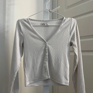 Vit ribbad långärmad topp från Hollister - Säljer en vit ribbad långärmad topp från Hollister med v-ringning och knappar framtill. Den har en tight passform och perfekt att styla till olika outfits🌺